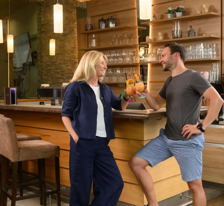 Zwei Gäste stoßen mit fruchtigen Cocktails an der Bar im Felsencafé des Bärenhofs Bad Gastein an – entspannte Stimmung in stilvollem Ambiente.