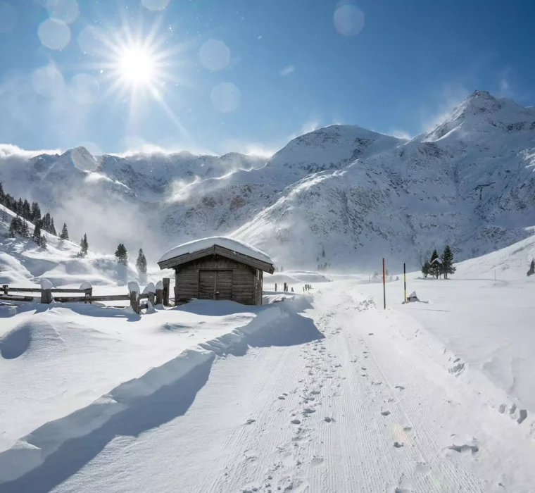 Winterliche Berglandschaft bei Bad Gastein mit verschneitem Holzhaus, Sonne und klar blauem Himmel im Gesundheitszentrum