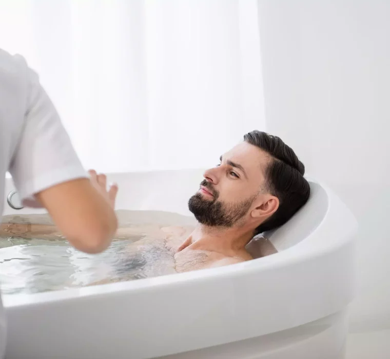 Mann entspannt in Badewanne im Gesundheitszentrum Bärenhof Bad Gastein bei therapeutischer Behandlung mit Pflegekraft